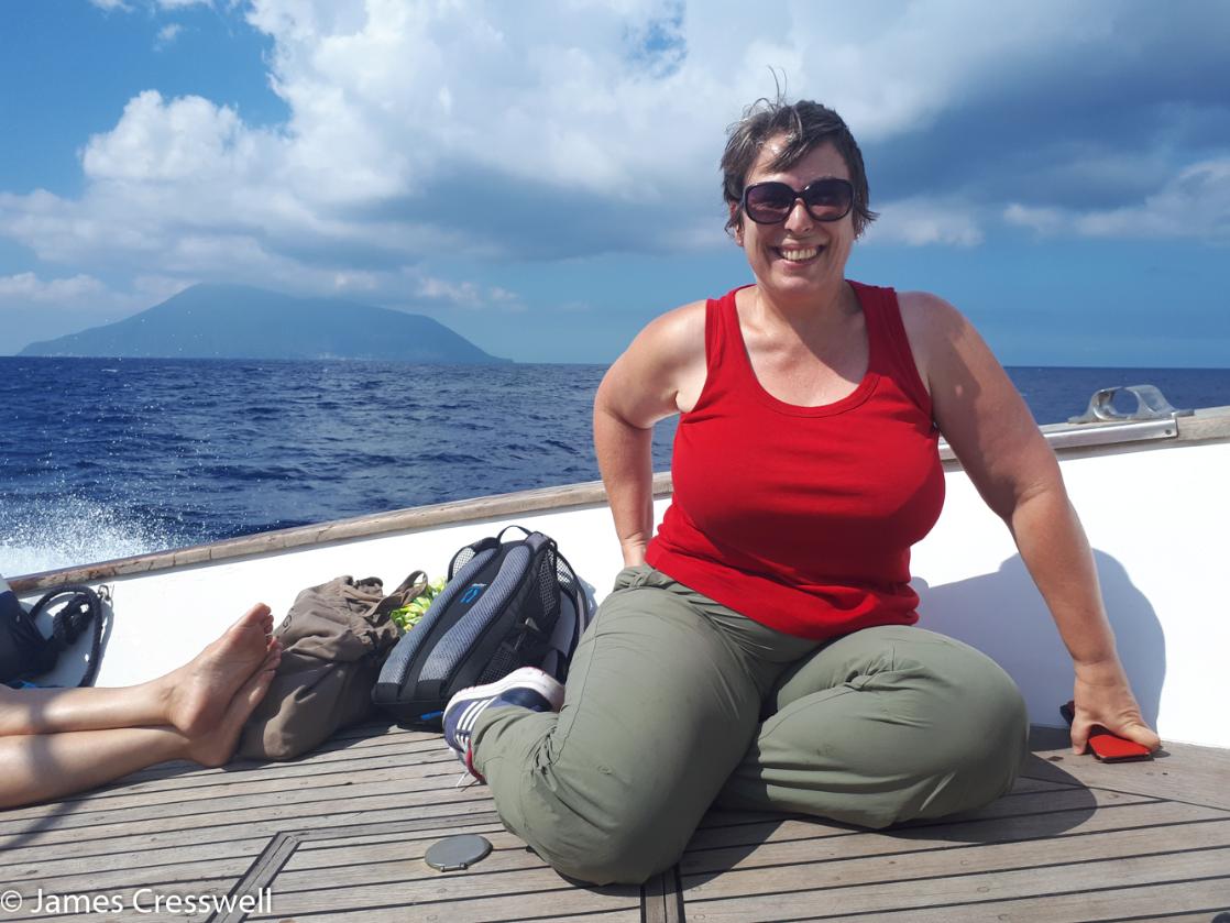 A photograph of a woman sitting on a boat with Stromboli volcano in the background taken on GeoWorld Travel's Italy volcanoes tour