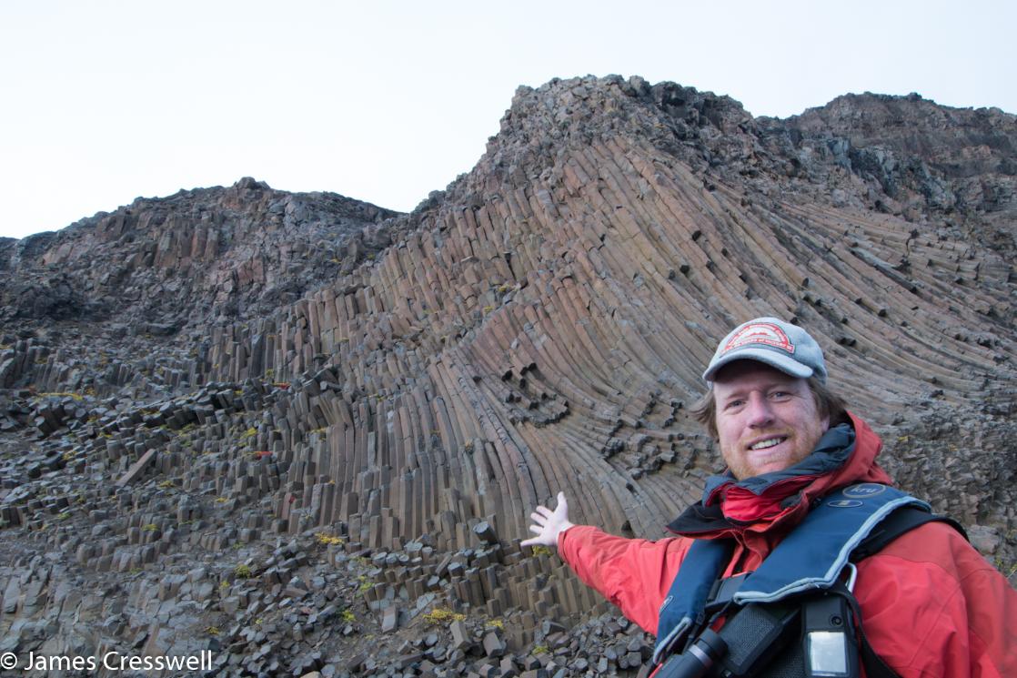 A photograph of James Cresswell pointing to columnar joints in East Greenland