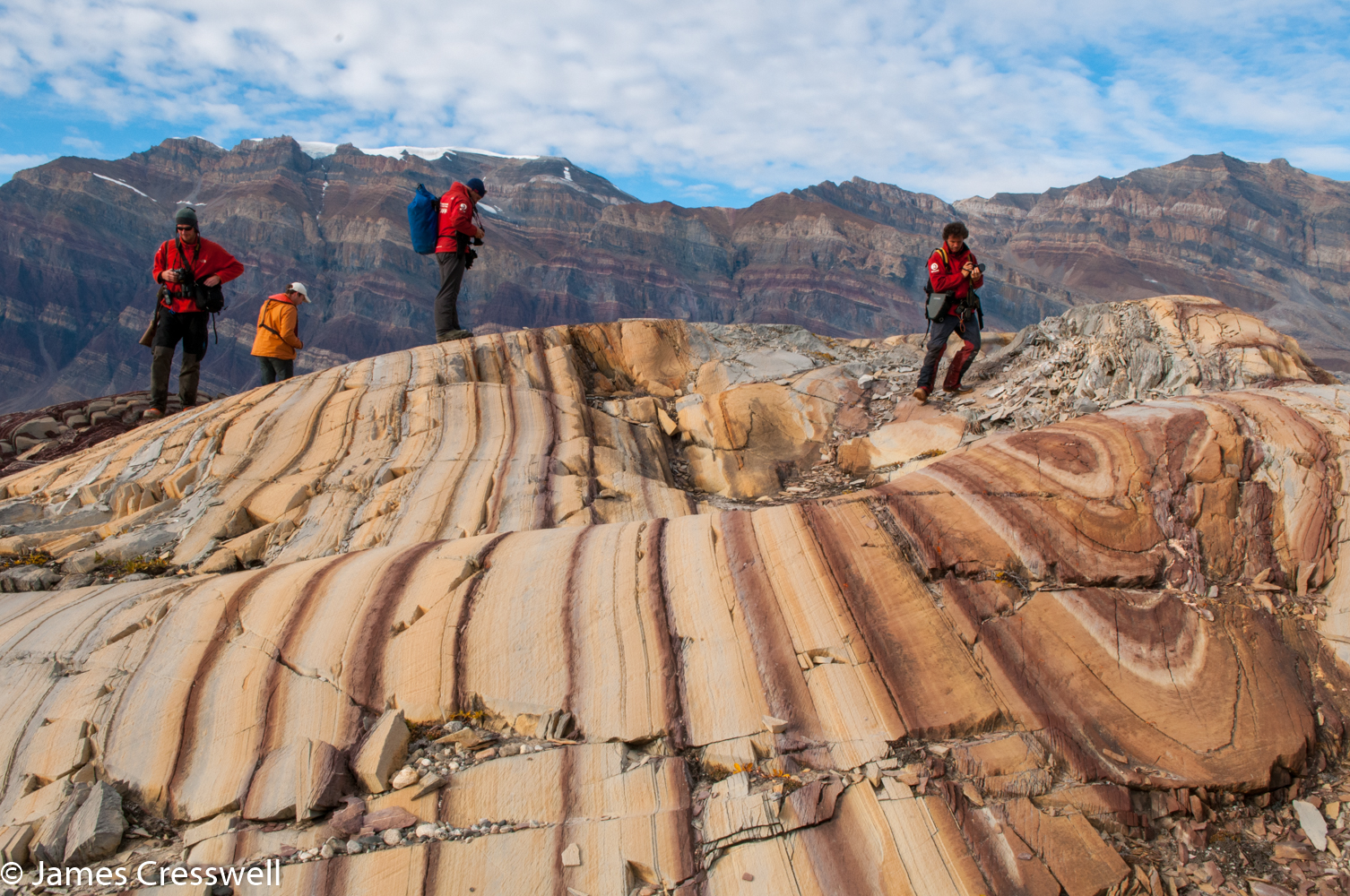 A photograph of people standing on stripy rocks taken in east Greenland on a PolarWorld Travel placed cruise