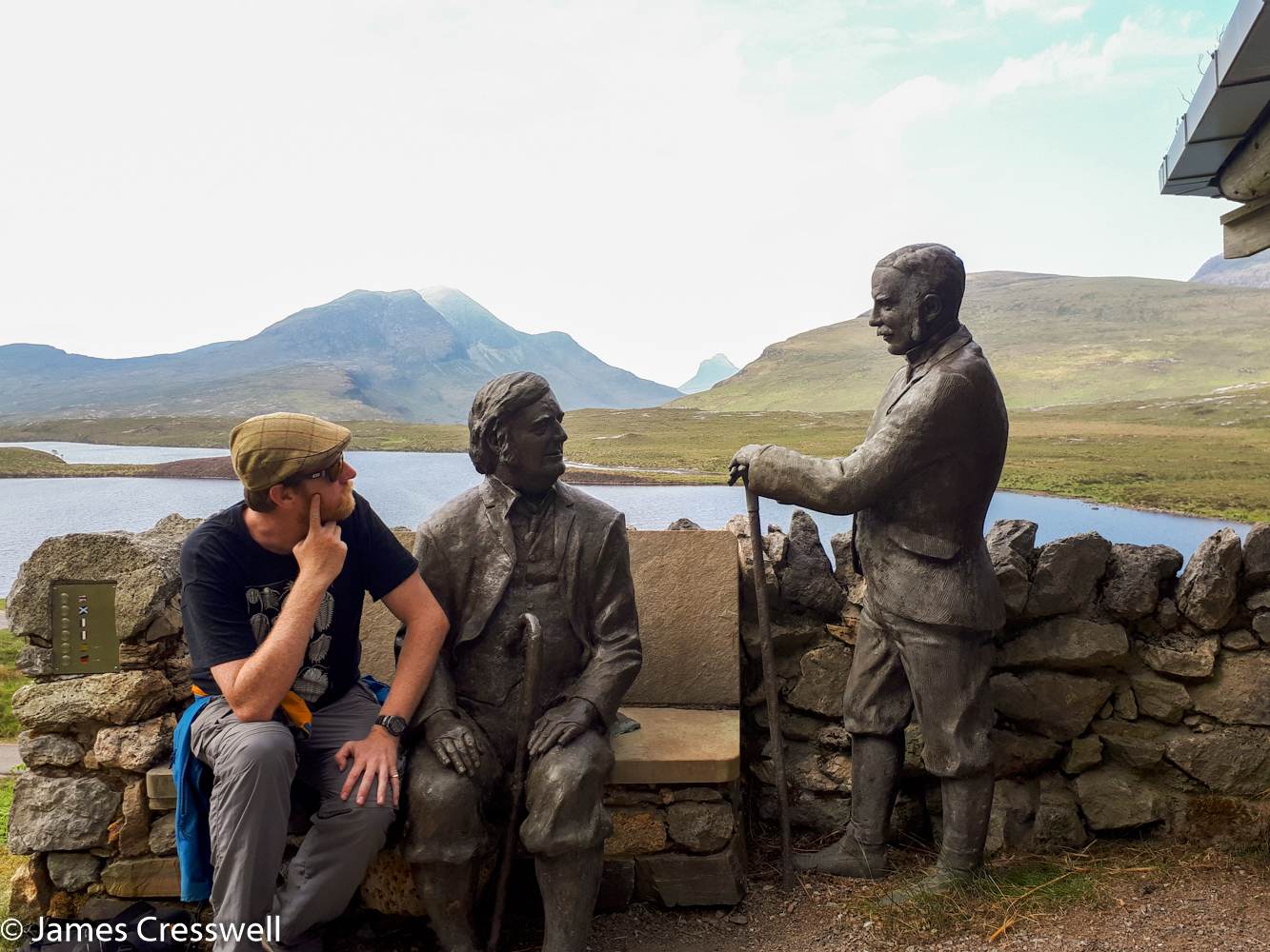 A photograph of James Cresswell with a statue of Ben Peach and John Horne at Knockan Crag, on a GeoWorld Travel History of Geology tour