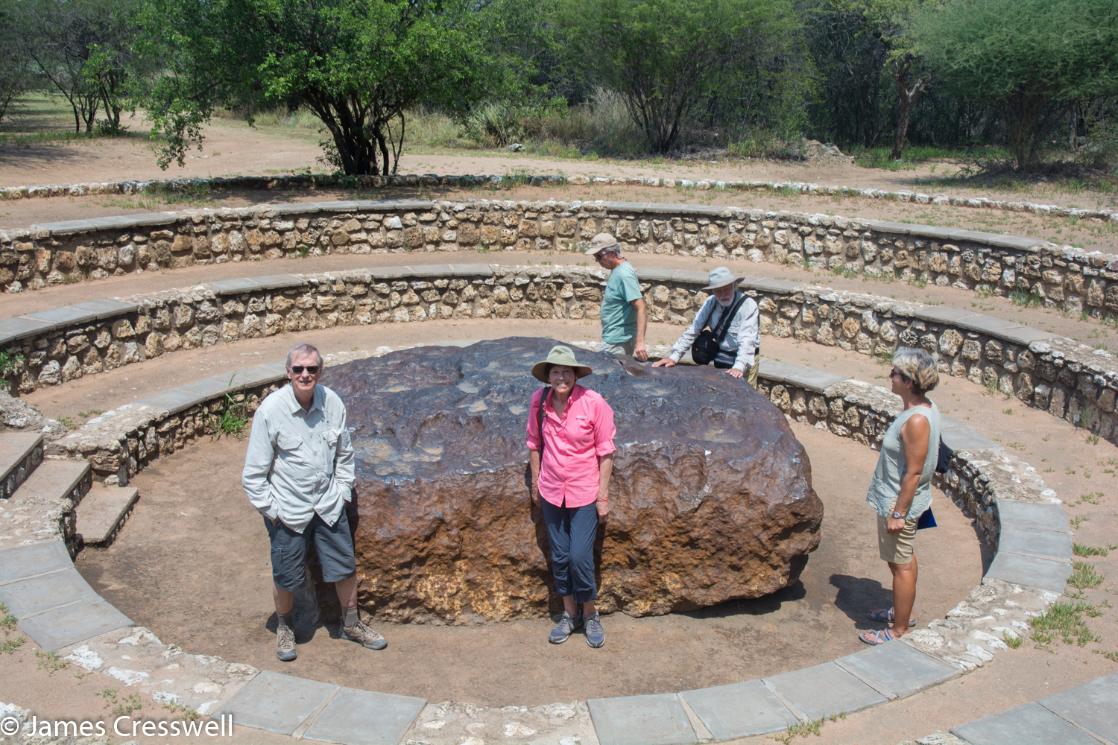 A photograph of five people standing around a huge iron meteorite, the Hoba Meteorite, taken on a GeoWorld Travel Namibia geology trip and tour