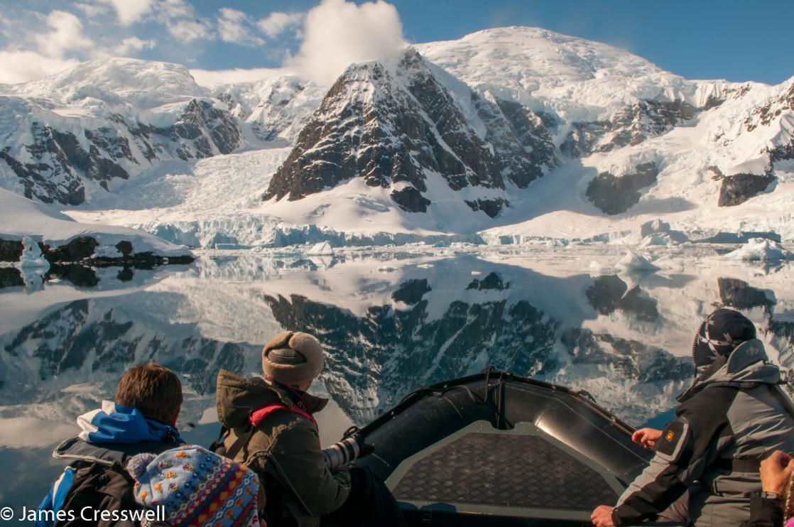 A photograph with people in the foreground admiring mountains in Antarctica, taken on a PolarWorld Travel placed expedition cruise