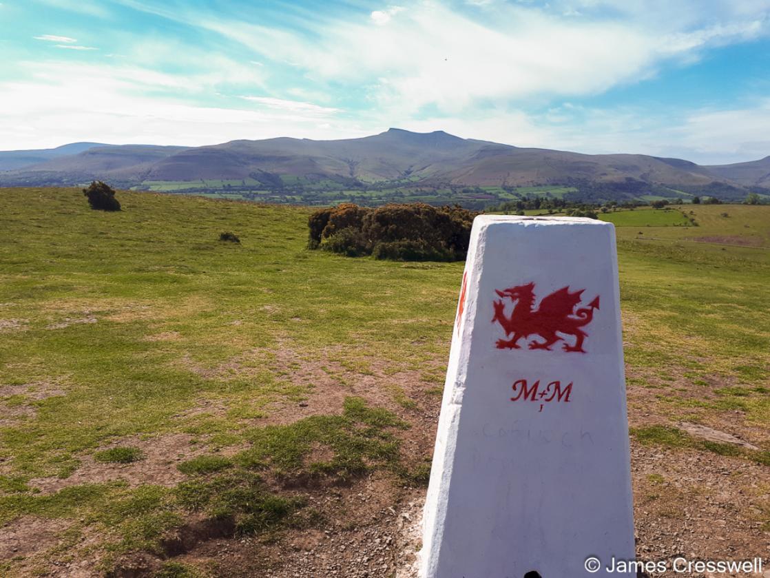 A photograph of a trig pillar and the Brecon Beacons mountains behind