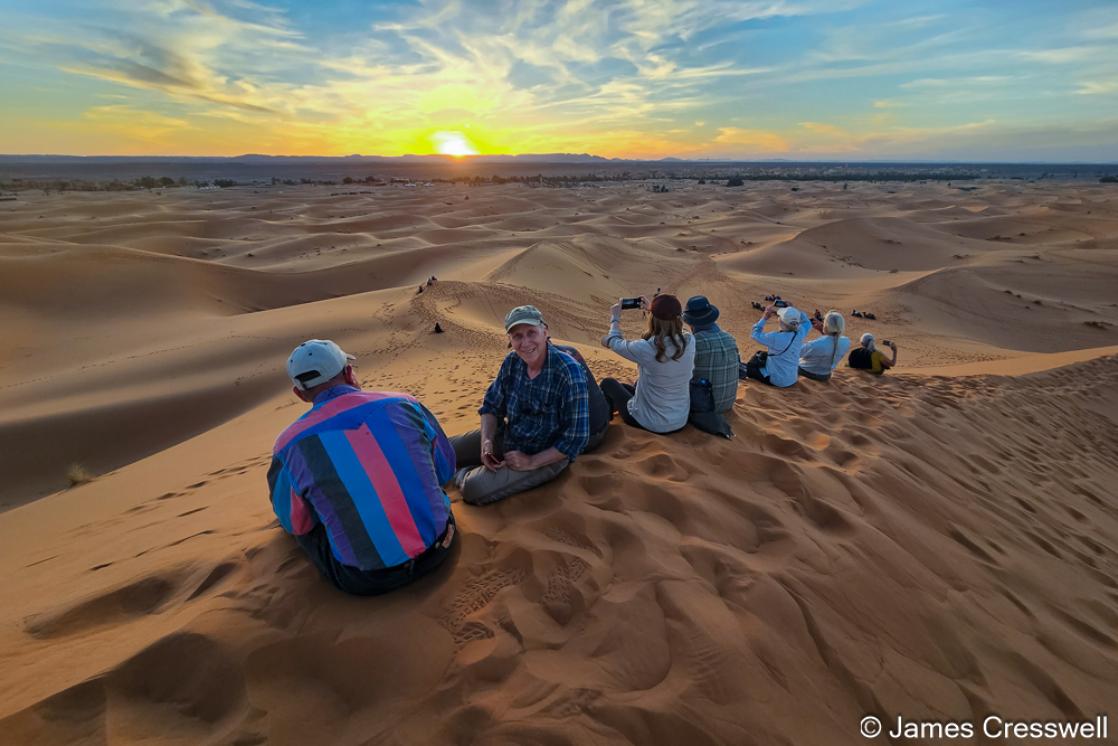 A photograph of a group of people watching the sunset in the Erg Chebbi sand dunes of Morocco